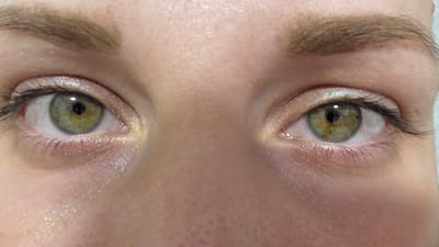 The image is a close-up, frontal view of a person's eyes. The irises are hazel with flecks of green and brown, and the pupils are black. Eyelashes are visible on both eyes, and there appears to be subtle eye makeup applied, including a light-colored shadow or highlighter on the eyelids. The skin around the eyes is fair with visible pores. The eyebrows are light brown and well-defined. The overall impression is a natural, unadorned portrait focusing on the eyes. There are no elements in the image that suggest a specific location in Sannikovo, Russia, or any other city.