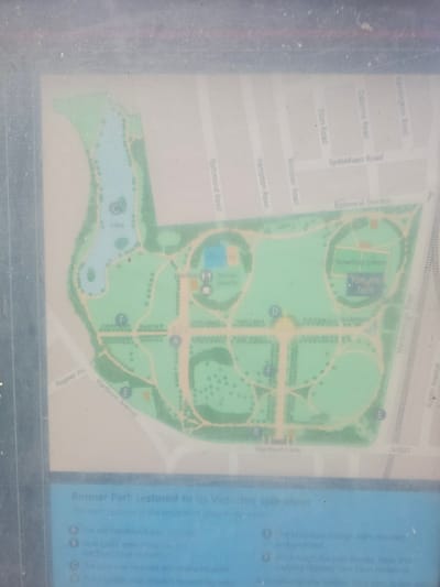 The image is a photograph of a laminated park map, likely an information board, set against a reflective, dusty surface. The map itself depicts "Ropner Park" in Stockton-on-Tees, United Kingdom, which has been restored to its Victorian splendor.

The map outlines the park's layout with green spaces, a blue lake labeled "lake" with a "C" marking, a playground, tennis courts, a bowling green, and a prominent sculpture. A "You are here" marker is visible near the bowling green. Several points of interest are indicated with letters: F, A, D, and E. Below the map, a legend describes restoration features, such as a bandstand, new gates, repaired lake drains, a restored fountain, boundary railings, replanted shrubs and trees, and a new pavilion with toilets. The map also shows surrounding roads like Ropner Av., Hartburn Av., Hartburn Lane, and A1027, as well as roads further afield like Richmond Road, Hampton Road, Windsor Road, Eton Road, Osborne Road, Sydenham Road, Balmoral Terrace, Kensington Road, and Austin Avenue. The overall condition of the map suggests it has been exposed to the elements and is showing signs of age and wear, with scratches and dust visible on its surface.