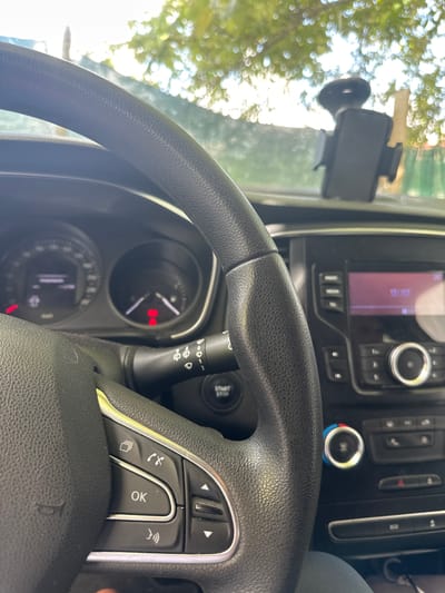 The image shows the interior of a car, focusing on the steering wheel and dashboard. A mobile phone holder is visible on the windscreen. The car's infotainment screen displays a digital clock. The dashboard includes buttons for the radio, media, and telephone. A start/stop button is located near the steering wheel. There is no indication of the location being Kashin, Bulgaria. No people are visible.
