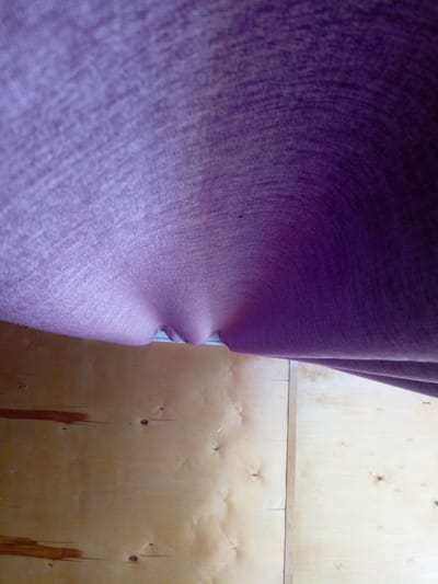 The image depicts a close-up view of a textured purple fabric that appears to be a curtain or draped material. The fabric is draped over a light-colored wooden surface, possibly plywood, which shows wood grain and some knots. The lighting suggests an indoor setting. There are no people or animals visible in the image. The image is oriented such that the fabric is in the upper portion, with the wooden surface below. The scene is generic and does not contain any discernible elements that would indicate a specific location within Churapcha, Russia, or any other city.