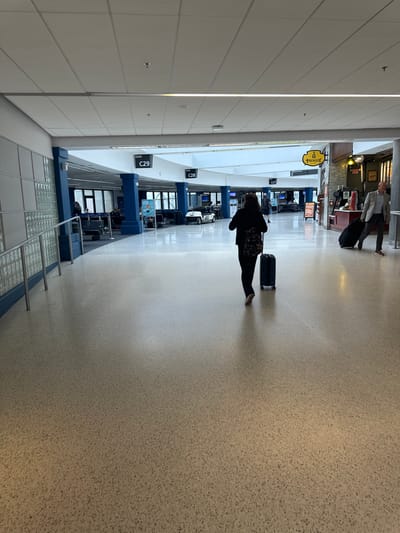 This image shows the interior of an airport terminal. A person is walking with a rolling suitcase in the C gate area. Overhead signage indicates gate numbers. The scene is likely in Cleveland, United States of America.