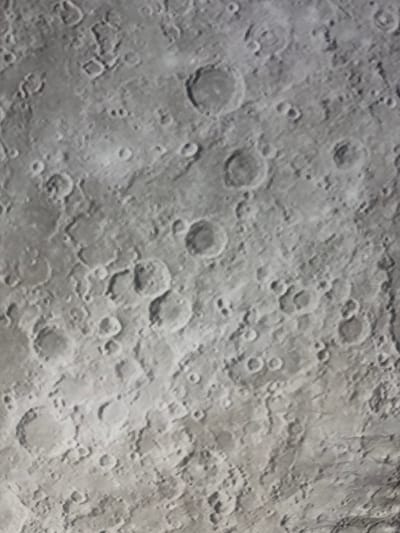 The image is a close-up, high-angle view of the surface of the Moon, showing numerous impact craters of varying sizes. The surface appears predominantly gray and textured, with shadows cast by the rims of the craters, indicating oblique lighting. There are no people, man-made objects, or any signs of life visible in the image. The environment is extraterrestrial and barren.
It is not possible to determine the location within the city of Baan Pang Ka, Thailand, as the image depicts the surface of the Moon.