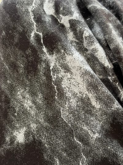 This image shows a close-up view of a dark fabric with a marbled or speckled pattern of white and light gray. The fabric appears to be creased and folded, creating shadows and highlights that emphasize its texture. There are no identifiable objects, people, or environmental features present. The image provides no information about the city of Hanniv, Ukraine, or any specific location within it.