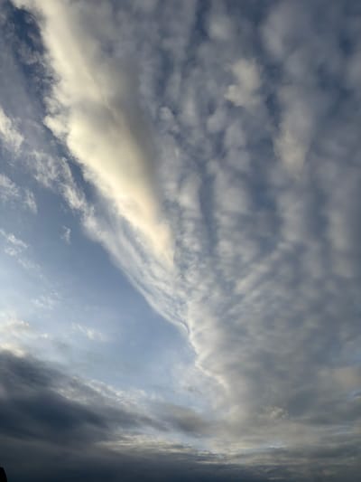 This image depicts a sky with a variety of clouds. The sky transitions from a clear, light blue on the left side to a more overcast and darker grey on the right. There are thin, wispy clouds that are illuminated by sunlight, creating a dramatic contrast against the darker, more textured clouds. The overall impression is of a dynamic and changing sky, possibly indicating an approaching weather front or the end of a day. There are no discernible landmarks or features that would indicate a specific location within the city of Naka, Laos. The image is a close-up of the sky itself, with no foreground or background elements visible that would provide geographical context.