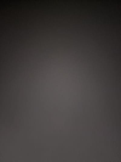The image is a full frame, high-angle shot of a plain, dark gray surface. The surface appears to be textured, possibly a wall or a fabric, with a subtle grain or speckled pattern visible throughout. There are no discernible objects, people, or actions depicted in the image. The lighting is uniform, with no distinct shadows or highlights, contributing to the overall flat and featureless appearance of the scene. The image is devoid of any contextual information that would place it in Burladingen, Germany, or any other specific location.