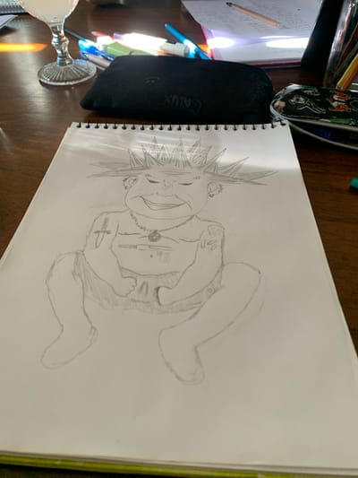 A pencil sketch of a cartoonish punk figure fills a spiral-bound notebook. The figure has a spiky hairstyle and multiple piercings. Details include tattoos, a necklace, and visible undergarments. The figure appears to be crouched or seated. The drawing is incomplete, with unfinished lines outlining the legs. The notebook sits on a wooden surface amidst stationery items like pens, pencils, and a case. A glass is also visible in the lower left corner.