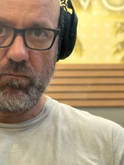 A close-up, skewed image shows a person wearing glasses and a black kippah. The person's gray beard and part of their face are visible, along with the corner of what appears to be a white garment, possibly a shirt or sweater. The background shows vertical slats and a yellowish pattern. There is no way to determine the location of this image based solely on visual elements of the photograph. It is not possible to determine if this image was taken in Duluth, United States of America.