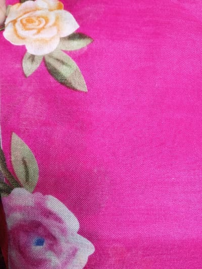The image features a close-up of floral fabric. A vibrant pink background dominates, textured with a visible weave. Two roses are partially visible, one in the top left corner with cream and yellow petals and green leaves, the other in the bottom left, mostly white with hints of pink and green leaves. The floral pattern contrasts with the solid pink backdrop.