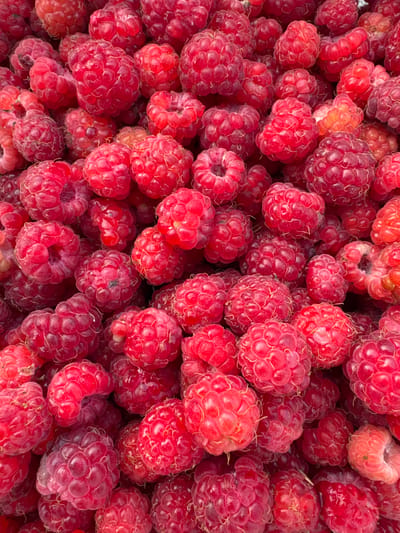 A top-down, close-up shot shows a large pile of fresh raspberries. The berries are a vibrant red and pink color, with some appearing slightly darker red. They are densely packed together, filling the entire frame of the image. The texture of the raspberries is clearly visible, with their characteristic bumpy, segmented surfaces. There are no people or animals visible in the image, and the background is entirely composed of more raspberries. The lighting appears to be natural, highlighting the rich colors and details of the fruit. There is no visible indication of the location being in the city of Красный Ключ, Russia; the scene is purely a depiction of the fruit.