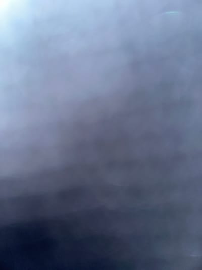 The image is a close-up, abstract shot of a gradient of colors, ranging from a bright, hazy white in the upper left corner to a deep, dark navy blue at the bottom. The texture appears soft and diffused, with no discernible objects or subjects. There are subtle hints of light flares or reflections, particularly in the upper right quadrant, exhibiting a faint rainbow hue. The overall impression is one of a smooth, atmospheric transition of light and shadow. No specific location within Bogorodskoe, Russia, can be identified from this image due to its abstract nature.