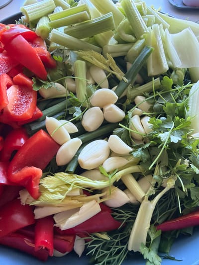 This image shows a close-up, overhead view of a collection of chopped vegetables in a blue bowl. The subjects are primarily food items: chopped red bell peppers, celery stalks, green onions, garlic cloves, and fresh herbs like parsley and dill. The scene is a still life, with no people or animals present. The focus is on the textures and colors of the raw ingredients, suggesting preparation for cooking or a meal.
There is no discernible activity taking place beyond the arrangement of the vegetables. The lighting appears to be natural, casting soft shadows and highlighting the fresh, vibrant colors of the produce. There are no clear indicators of the time of day, weather, or specific location within Aespa, Estonia, other than the blue bowl itself. The mood conveyed is one of freshness and potential, associated with food preparation. No text is visible in the image.