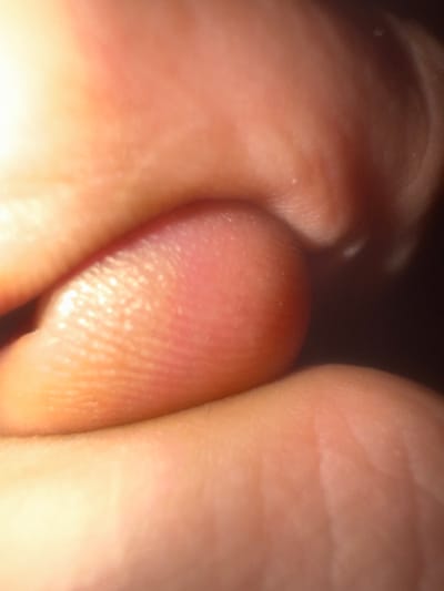 The image displays an extreme close-up of human skin, specifically the pad of a digit, likely a finger or thumb. The skin exhibits typical dermatoglyphics, characterized by distinct fingerprint ridges and valleys, particularly prominent in the lower-left to central portion. The coloration of the skin ranges from pale pink to reddish-orange and amber tones, with areas of highlight suggesting direct light illumination from the upper-left, and darker regions indicating shadow, defining the curvature of the digit. Multiple subtle folds and fine lines are visible across the skin surface, consistent with epidermal texture. No other subjects, objects, or environmental details are present. The precise location within the city of Southampton, United Kingdom, cannot be determined from the visual content of this image.