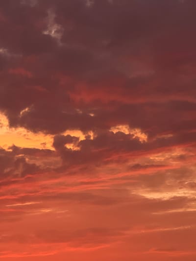 The image depicts a dramatic sky filled with clouds during what appears to be sunset. The clouds are a mixture of deep purples, reds, oranges, and yellows, suggesting intense atmospheric conditions and lighting. There are no discernible landmarks or specific features that would place this image within the city of Rotmanka, Poland. The scene is entirely composed of the sky and clouds, with no human presence or man-made objects visible.