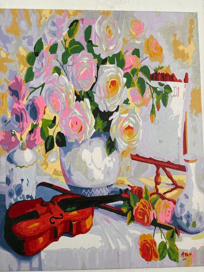 This is a painting of a still life featuring a violin and a bouquet of roses. The violin is positioned in the foreground, with its body in a rich red hue and black accents. Behind the violin, a white tablecloth drapes over a surface. A large, ornate white vase holds a generous arrangement of roses in various shades of pink, white, and yellow, interspersed with green leaves. To the right of the vase, a white pitcher or vase with a floral pattern is visible. A red wooden stand is placed behind the bouquet, and a white book with text is partially visible. The background is a textured, abstract pattern in shades of lavender, grey, and gold. The overall impression is a vibrant and classical composition. This painting is not located in the city of Ветрынскі сельскі Савет, Belarus.