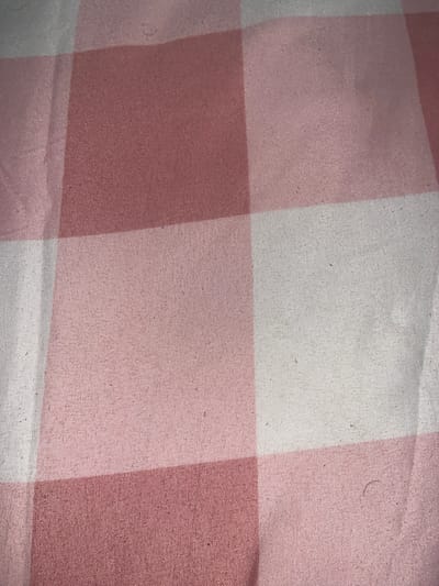 The image shows a close-up of a pink and white checkered fabric, likely a tablecloth or bedding. The fabric has a woven texture with small imperfections and lint visible. The image does not provide any information about its location in Lambaro Kueh, Indonesia, or any context related to people, actions, or interactions. It is a purely visual representation of the material.