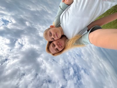 In Breytovo, Russia, a woman with blonde hair is holding a child, who is resting his head on her shoulder. They are both looking at the camera. The background is a sky filled with clouds.
