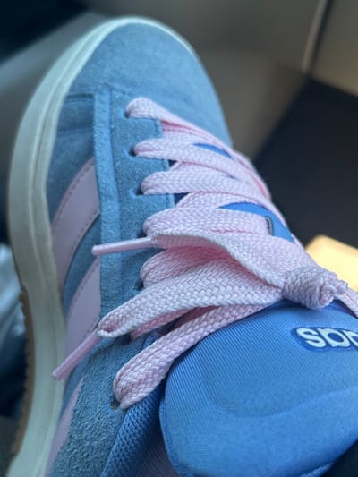 A close-up, side-view image shows the top of a light blue Adidas sneaker with pink laces. The shoe has light pink stripes on the side. The sneaker is worn and appears to be in a vehicle, possibly a car, as indicated by the dark, blurred background which suggests a seat or interior. The laces are tied in a knot. The Adidas logo is visible on the tongue of the shoe. The image does not provide any information about the city of Everett, United States of America.