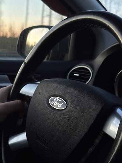 A close-up image shows the steering wheel of a Ford vehicle. The Ford logo is visible in the center of the steering wheel. A ventilation vent is visible behind the steering wheel. The image does not provide any information about the location of Yoksolovo, Russia, or any people or actions.