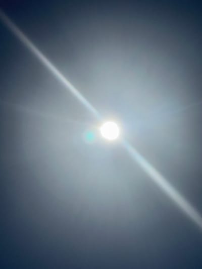 The image shows a bright light source, likely the sun, obscured by haze or thin clouds. A diagonal streak of light emanates from the central point. The background is a muted grey-blue, suggesting the sky. The location is Unknown, France.