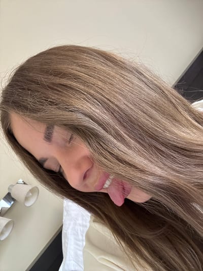 A woman with light brown hair is sticking out her tongue. The background includes a bed, a wall, and light fixtures. The image does not contain enough information to determine the location is in Sosnovy, Russia.