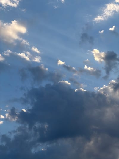 The image is a low-angle shot of a sky with a mixture of dark and light clouds. The sky is a light blue color, visible in patches between the clouds. The clouds range from puffy white clouds with sunlit edges to dense, dark gray storm clouds. Some faint streaks of light can be seen through thinner cloud formations. There are no people, subjects, objects, actions, or interactions visible. The environment is solely the atmospheric conditions of a sky. The location in the city of Pentre, United Kingdom, is not definitively confirmed by the image.