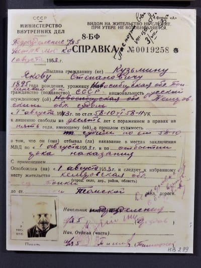 The image is a scan of a Soviet internal passport, likely issued in the 1950s. The document is predominantly text with some handwritten entries. The top section has official stamps and seals, including "CCCP" and "МИНИСТЕРСТВО ВНУТРЕННИХ ДЕЛ". There is a small black and white photograph of an elderly man with a mustache and a goatee, wearing a dark suit and a medal. His left hand is visible, resting on the bottom edge of the frame.
The handwritten text appears to be personal details and legal information related to the passport holder. Some legible entries include: "1895 года рождения", "уроженцу (кой)", "гражданство (подданство) СССР", and information about criminal proceedings and imprisonment. There are also sections for the holder's place of residence and release details.
A key piece of handwritten information is "месту жительства ... kemi, ob." (place of residence ... Kemi, ob.) and "до ст. ... Torcкu ... Toмcku" (to station ... Tocki ... Tomsk). This suggests that the individual was released and possibly relocating to or from the region of Tomsk, Russia. The city of Ust'-Pyzas is not explicitly mentioned in the visible text.