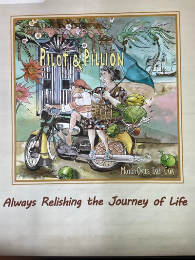 The image depicts a stylized illustration of a "Pilot & Pillion" scene, likely representing a motorcycle taxi service in Goa, India, as indicated by "Motor Cycle Taxi Goa". The illustration shows a man and woman riding a yellow and black motorcycle, overloaded with goods, possibly including coconuts and other produce. The environment includes palm trees and a building rendered in a whimsical, watercolor style. The phrase "Always Relishing the Journey of Life" is printed to the side. The specific location in the city of Kasarvarne is not depicted in the image.