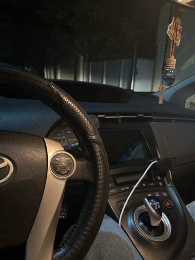 The image shows the interior of a car at night. The steering wheel, dashboard, and gear shifter are visible. A car air freshener is hanging from the rearview mirror. The exterior environment is dark, suggesting it is nighttime, with some trees and lights visible through the windows. The location is identified as Gaidar, Moldova.