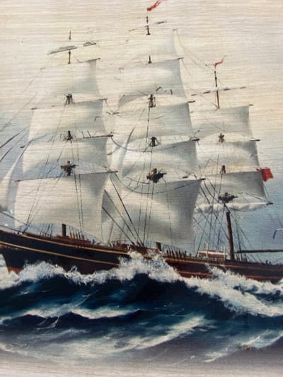 The image depicts a tall ship sailing through rough waters. The ship has multiple sails fully extended and is riding a large wave. The hull is dark, contrasting with the white sails and foamy waves. The sky is light, suggesting a bright day. The image appears to be a painting or print on a wooden surface, indicated by the wood grain visible in the background. There is no information provided suggesting the location in the city of Krasnoyar, Russia, or any other specific geographic context.