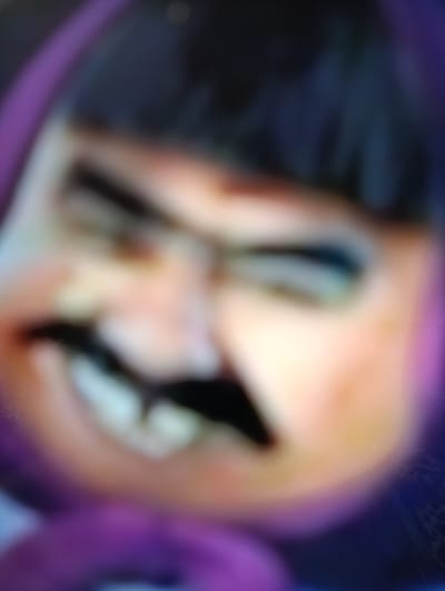 This is a close-up, heavily blurred media file featuring a cartoon character. The subject is a face with dark hair, a prominent black mustache, and fair skin with rosy cheeks. The character appears to be wearing a purple hooded garment. The expression conveyed is a wide, toothy grin, with the eyes squinted in what could be interpreted as malicious amusement or excitement. The background is dark and indistinct, with hints of purple and blue hues. The image quality is poor, with significant blurriness obscuring fine details, suggesting it may be a low-resolution capture or a screenshot from a video. There are no discernible objects, setting details, time of day, weather, or visible text that can be identified due to the severe lack of clarity. The overall impression is that of a stylized, possibly villainous, animated character.