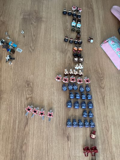The image shows a collection of miniature figurines and accessories arranged on a wooden surface. The items appear to be organized into rows or groups based on their type or design. At the top left is a pale pink slipper and a small floral patterned purse. A group of Stranger Things figurines including Dustin, Eleven and Will are on the left. Demogorgons are located to the right of the figures, with a single Demogorgon hairclip above 4 others.
To the right are blue figures of an unknown type, and to the right of them, red figures.
At the bottom left, partially obscured, is a collection of Minecraft characters.
The image does not provide any information to determine a specific location in Fulda, Germany, or any other geographic location.