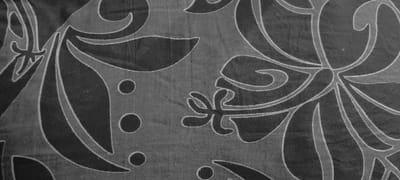 A close-up, black and white image of a fabric with a patterned design. The fabric has a floral pattern, with large, stylized leaves and flowers. The leaves are dark and have white outlines. The flowers are white and have a dark center. The background is a light gray. The fabric is likely from a house or a clothing item. The location is Punaauia, French Polynesia, at coordinates -17.604, -149.619.