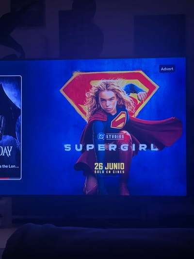 The media file is a promotional image for the movie "Supergirl." The central subject is a young woman, dressed in a blue and red Supergirl costume with a yellow S-shield on her chest. Her blond hair is disheveled, and she appears to be in motion, leaning back with her cape flowing dramatically behind her. The background is a vibrant blue with a yellow and red spray-painted S-shield.

Visible text includes "ADVERT" in a small white box at the top left. Below the image of Supergirl, there is text that reads "STUDIOS" and "SUPERGIRL." Further down, it says "26 JUNIO SOLO EN CINES," which translates to "June 26th In Cinemas Only."

The overall mood is energetic and heroic, fitting for a superhero movie poster. The lighting suggests a dramatic presentation, likely on a screen or as a printed poster. The "Advert" label indicates this is a promotional advertisement. The text "SOLO EN CINES" suggests the movie is intended for theatrical release. The date "26 JUNIO" places the release in June, and given the Spanish text, it's likely for a Spanish-speaking market. The location context of Mollet del Vallès, Spain, confirms the Spanish release.