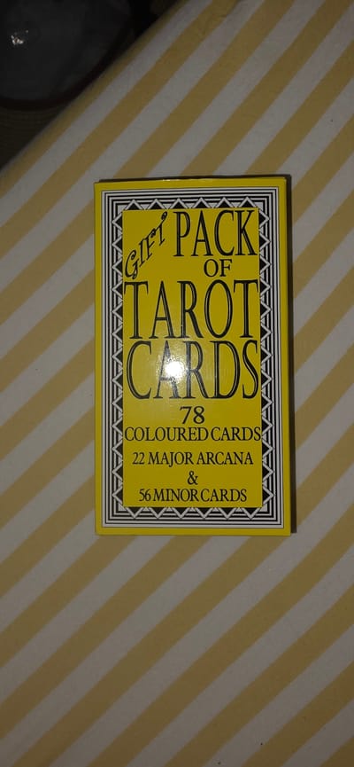 The image shows the top view of a gift pack of tarot cards. The pack is yellow with black lettering. The text on the pack reads "GIFT PACK OF TAROT CARDS" in large fonts, and below that, "78 COLOURED CARDS 22 MAJOR ARCANA & 56 MINOR CARDS". The pack is placed on a surface with diagonal yellow and white stripes. There is no discernible information or context to suggest any connection to Lieli, Switzerland.