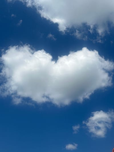 The image captures a bright blue sky with scattered white clouds. The perspective is looking upwards, giving a sense of vastness. In the upper right corner, a sliver of a red tiled roof is visible, suggesting the presence of a building. The clouds are varied in size and shape, with some appearing dense and billowy, while others are wispy and spread out. The overall impression is of a clear, sunny day, likely during daylight hours given the illumination of the clouds. The scene is devoid of people or specific objects other than the hint of the rooftop. No text is visible in the image. The location context of Lopaskyne, Ukraine, provides a geographical reference for the scene.