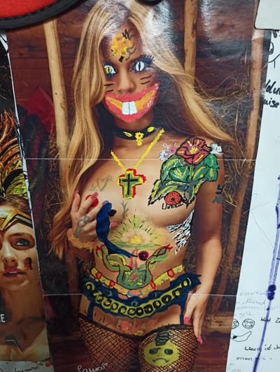 The image displays a collage of photographs and drawings, with a prominent central image of a woman whose body and face have been painted with various designs. The woman has blonde hair and is wearing black fishnet stockings. The painted elements include a large red and yellow smile with white teeth on her face, blue and yellow eye makeup, a yellow necklace with a cross pendant, and floral designs on her chest. Her body is also adorned with abstract shapes and figures. To the left of the central image, a portion of another photograph shows a woman's face with elaborate headdress-like makeup. To the right, there are handwritten notes and drawings on white paper. The background of the central image appears to be a rustic setting with wooden beams. The collage is affixed to a surface, and there is a red border at the top. There is no information available in the image to indicate its location in the city of Werl, Germany.