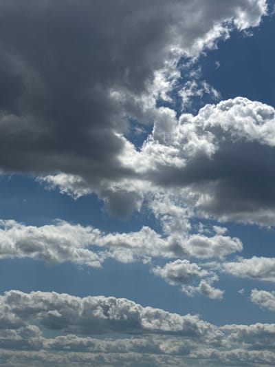 This media file shows a dramatic skyscape with a variety of clouds. The dominant subjects are formations of cumulus clouds, some dark and heavy with what appears to be rain, and others bright white and fluffy. The clouds are arranged in distinct masses, with a large, dark cloud dominating the left side of the frame, and lighter, more textured clouds stretching vertically on the right. The background is a clear blue sky, suggesting it is daytime.
The weather appears to be dynamic and possibly unsettled, given the presence of the dark storm cloud. The light suggests it is daytime, with the sun likely high in the sky, illuminating the edges of the white clouds. There are no specific location cues in the image itself, but the provided location context is Акцябрскі сельскі Савет, Belarus. No people or man-made objects are visible, and there is no visible text. The scene evokes a sense of the power and beauty of nature, with the contrasting cloud formations creating a visually striking image.