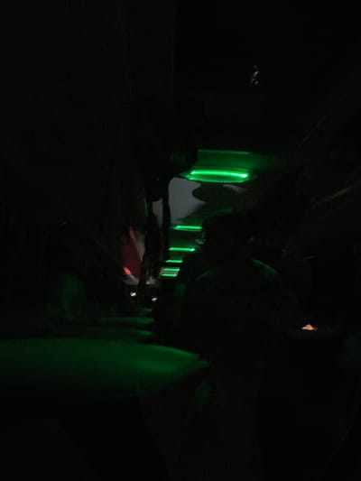 A dimly lit interior of a vehicle, likely an airplane, at night. Green lights highlight the edges of the passenger windows. The red light suggests a signal or display. The location of Lesichovo, Bulgaria is not determinable from visual information.