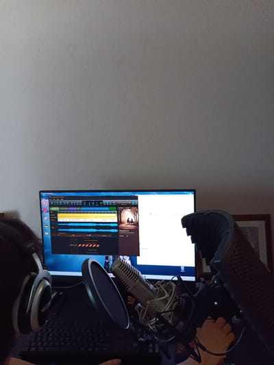 An indoor scene features a computer monitor displaying audio editing software. A microphone with a pop filter is positioned in front of the monitor, and a person wearing headphones is partially visible on the left side of the image. The monitor shows audio waveforms and track information, suggesting music production or recording activities. The background is a plain wall. The specific location within Évreux, France, cannot be determined from the image.