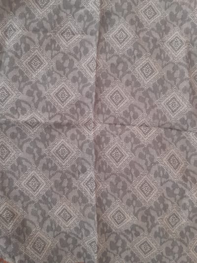 The image shows a close-up, overhead view of a gray fabric with a repeating diamond pattern. The pattern features intricate geometric designs within each diamond, interspersed with abstract, organic shapes. The fabric appears to be a textile, possibly a scarf, tablecloth, or upholstery. The lighting is even, and the texture of the fabric is visible, suggesting it is woven. No people, animals, or specific landmarks are visible. The location in Bayaut, Uzbekistan is not discernible from the visual information presented in the image.