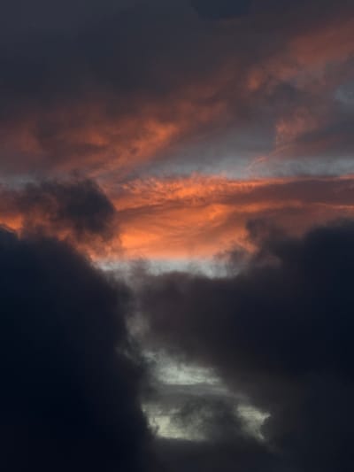 This image captures a dramatic cloudscape over Fécamp, France, likely at sunset or sunrise due to the distinct lighting. The sky is dominated by a striking contrast between brightly illuminated clouds and heavy, dark formations. A prominent vertical band of clouds on the left-center is bathed in vivid orange and reddish hues, with some sections appearing silvery-white. This brightly lit segment stands out against expansive areas of deep blue-grey to almost black clouds, which occupy the right side and other parts of the frame, suggesting a dense cloud cover. The interplay of intense natural light and deep shadow creates a dynamic and powerful visual. There are no people, identifiable objects, or visible text in the image.