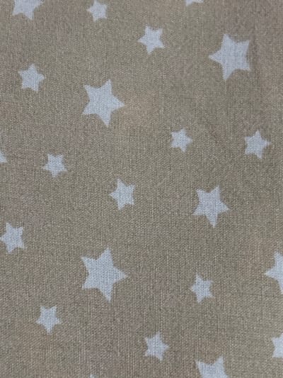 The image displays a close-up, overhead view of a beige fabric with a repeating pattern of white, five-pointed stars. The fabric appears to be a woven material, possibly cotton or a blend, with a visible texture of vertical and horizontal threads. The stars vary slightly in size and are distributed randomly across the fabric. There are no people, animals, or any other objects present in the image besides the fabric itself. The lighting is even, suggesting an indoor setting with diffused light. The image does not contain any information that would allow for the identification of its location within the city of Jrarat, Armenia.