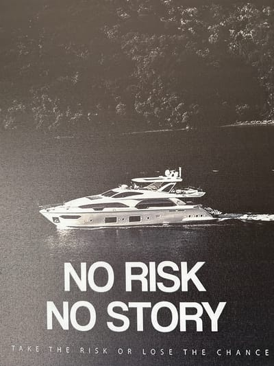 The media file is a black and white image of a yacht sailing on dark water. The yacht is the main subject of the image, positioned to the right of the frame. It appears to be a modern, sleek vessel with multiple levels and windows. The water is dark and choppy, suggesting movement and possibly rough conditions. The overall scene is stark and dramatic, with a high contrast between the white of the yacht and the black of the water and background.
Prominently displayed on the right side of the image, oriented vertically, is bold white text. The text reads "NO RISK NO STORY" on two lines, with "NO RISK" above "NO STORY". Below this, in smaller text, also oriented vertically, is the phrase "TAKE THE RISK OR LOSE THE CHANCE". The text is clear and impactful, serving as a strong motivational or cautionary message.
There are no people visible in the image. The setting appears to be open water, likely at sea or on a large body of water. Given the context of Oldham, United Kingdom, it's possible this is a promotional image for a marine-related business or event. The time of day and weather are not explicitly indicated, but the dark water and lack of sunlight suggest it could be overcast, at dusk, or simply a moody shot. The overall emotion conveyed is one of ambition, adventure, and the potential for reward through taking risks.