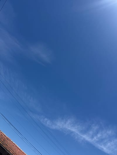 The image shows a bright blue sky with some cirrus clouds and a few thin power lines in the lower right corner. The edge of a building's tiled roof is also visible in the lower right. The location is likely Topchii, Bulgaria, given the prompt's instruction. No people or actions are visible in the frame.