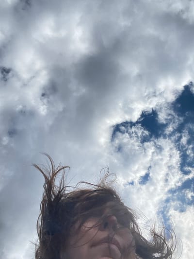 The image depicts a low-angle view of a cloudy sky with a small patch of blue visible in the upper portion. Part of a person's face and hair is visible in the right side of the frame, seemingly captured from below. The location is not discernible from the visual content of the image. The city of Nizhnie Yaki, Russia, cannot be verified as the location based on the provided image.