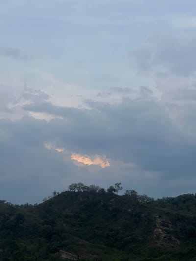 The image shows a view of the sky with clouds and the silhouette of a forested mountain ridge on the right. The sky is mostly overcast with varying shades of gray and some hints of light breaking through the clouds. The mountain ridge is dark green, with visible trees along the top. There is no indication of location in Gracias, Honduras or any people, subjects, objects, actions, or interactions.