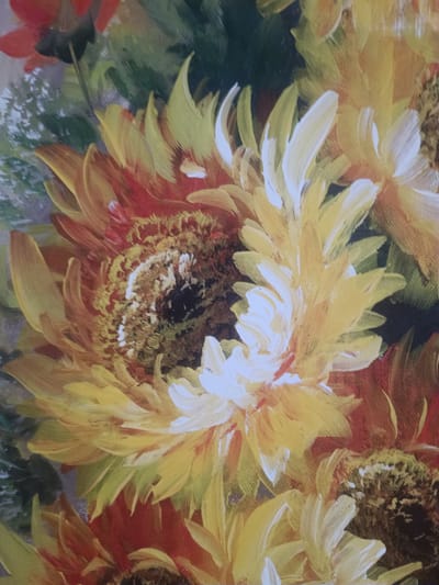 The image is a close-up, detailed oil painting of sunflowers. The painting features a vibrant bouquet with a central, large sunflower dominating the foreground. Its petals are a mix of bright yellow and orange, with hints of red at the base. The center of this sunflower is dark brown and textured, suggesting seeds. Surrounding it are other sunflowers, some fully bloomed and others partially visible, displaying similar color variations. White highlights on the petals create a sense of light and depth. In the background, hints of green foliage and other floral elements add depth to the composition. The painting style is expressive and textured, with visible brushstrokes. The image does not depict any elements related to the city of Mezhgorye, Russia.