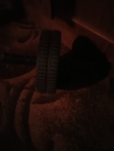 The image shows a close-up view of two Oreo cookies placed on a textured orange blanket. The cookies are stacked on top of each other, with their ridged edges visible. The lighting is dim, casting long shadows and obscuring some details of the surrounding environment. The scene appears to be indoors, possibly in a home setting in Yermilovo, Russia. There are no people or other objects clearly identifiable in the image besides the cookies and the blanket.