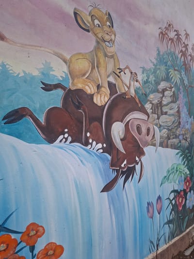 The image is a painting of the Lion King characters Timon, Pumbaa, and Simba. They are set against a background depicting a jungle scene on the left and a waterfall and flowers on the right. The painting is likely on a wall or other flat surface. There is no indication that this image is related to the city of Debnevo, Bulgaria.