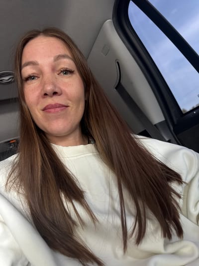 A woman with light skin and long brown hair is in a car. She is wearing a white sweatshirt. The car appears to have a sunroof. The location is unknown, but not confirmed to be in the city of Можга, Russia. There are no other people, objects, actions, or interactions directly visible in the image.